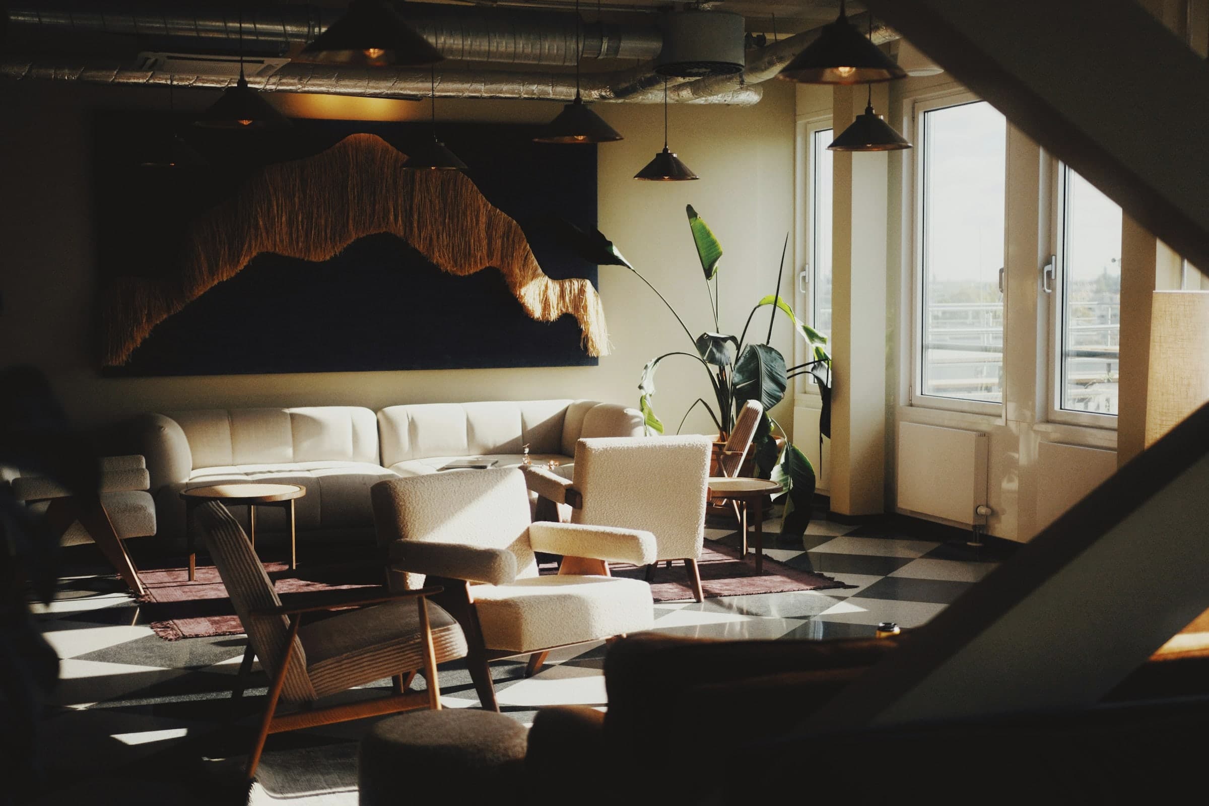 Lounge in einem Büro mit hellen Sofas, Bouclé-Sesseln und einem großen Wandtextil im Nachmittagslicht